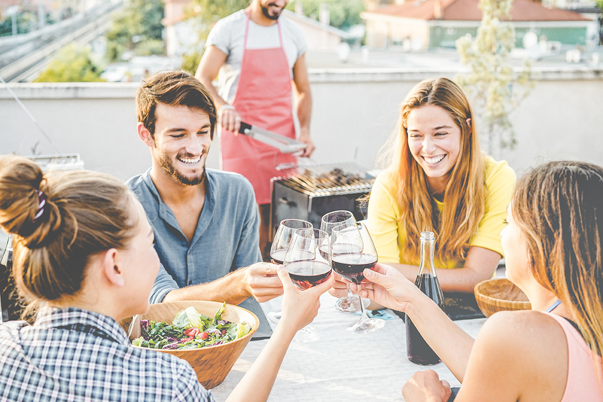 Happy friends cheering with red wine at barbecue dinner party -